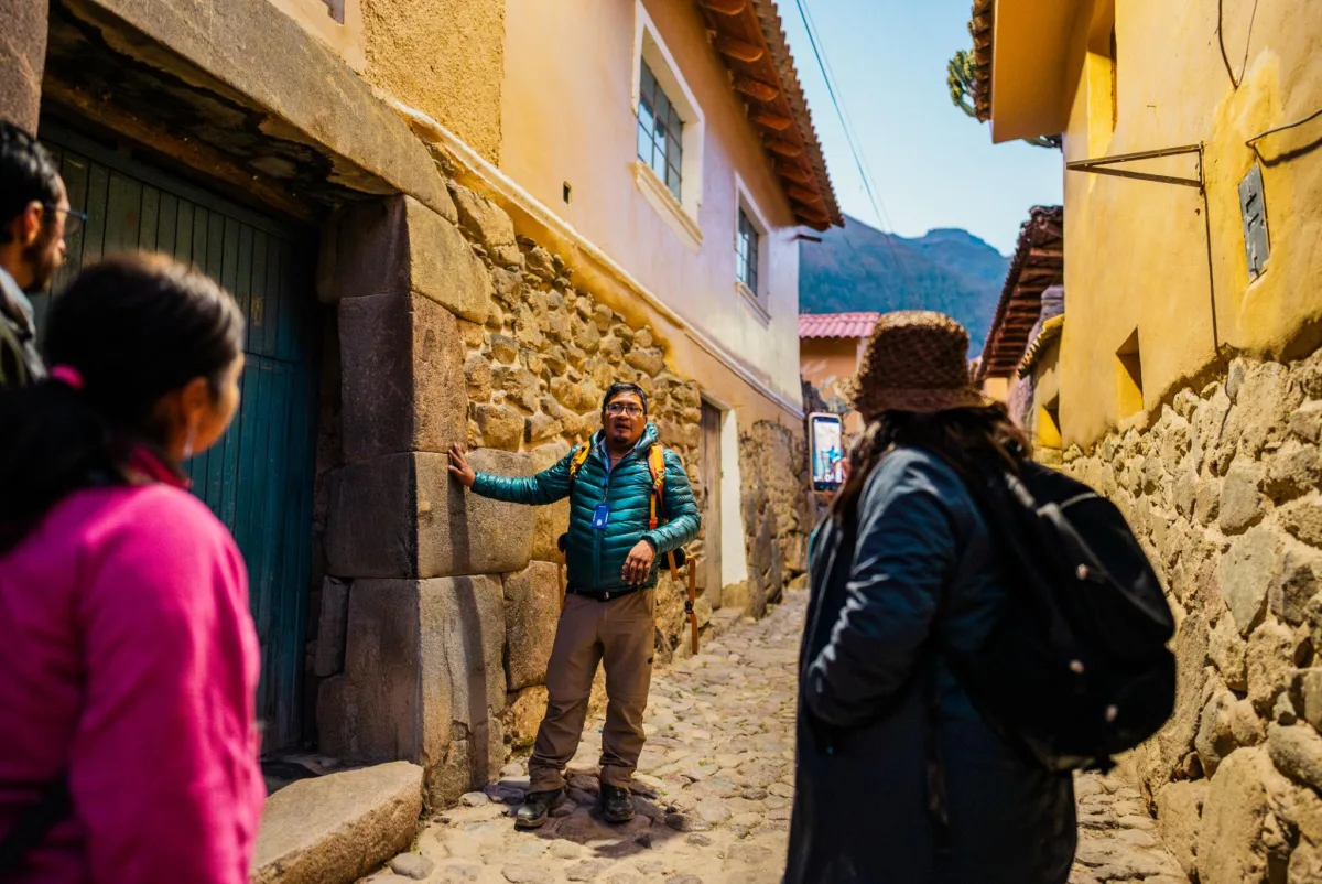 Guía explica la arquitectura de piedra ancestral a viajeros en un callejón histórico de los Andes.